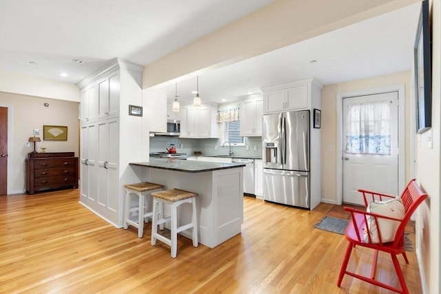 kitchen with a peninsula, appliances with stainless steel finishes, dark countertops, and light wood-style floors