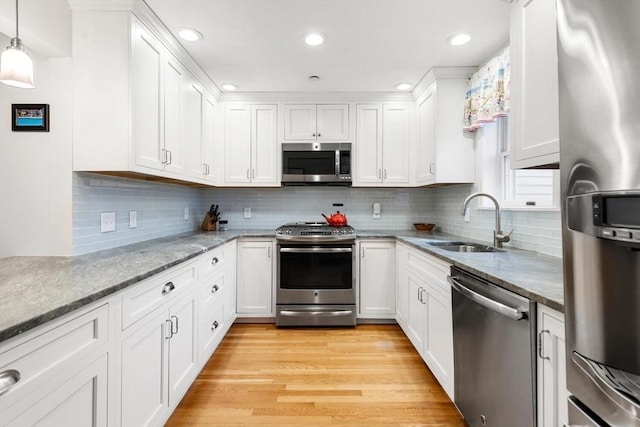 kitchen with light wood finished floors, appliances with stainless steel finishes, a sink, and white cabinetry