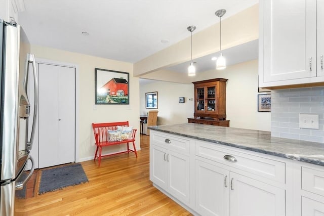 kitchen with light wood finished floors, backsplash, freestanding refrigerator, white cabinetry, and light stone countertops