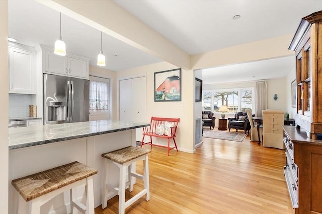 kitchen featuring stainless steel fridge with ice dispenser, light wood-style flooring, a breakfast bar, stone counters, and white cabinetry