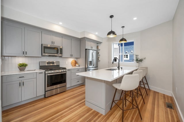 kitchen with appliances with stainless steel finishes, gray cabinetry, pendant lighting, light wood-type flooring, and sink