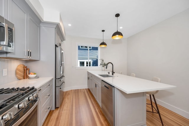 kitchen featuring hanging light fixtures, sink, gray cabinets, stainless steel appliances, and a breakfast bar