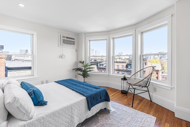 bedroom featuring baseboards, a wall mounted AC, multiple windows, and wood finished floors