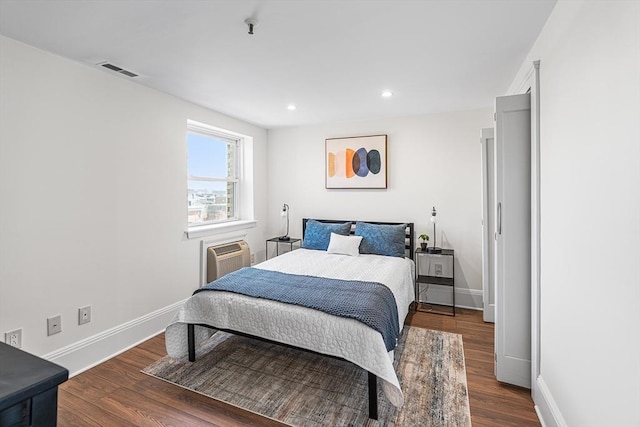 bedroom with visible vents, wood finished floors, baseboards, an AC wall unit, and recessed lighting
