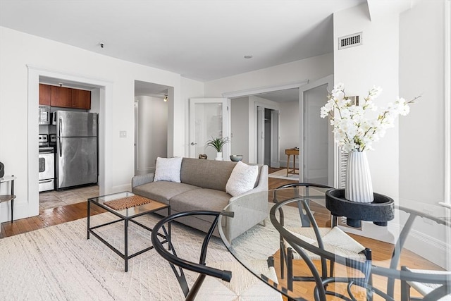living room featuring visible vents, light wood finished floors, and baseboards
