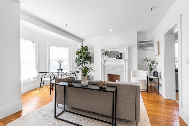 living area featuring a high end fireplace, baseboards, a wall unit AC, and light wood-style floors