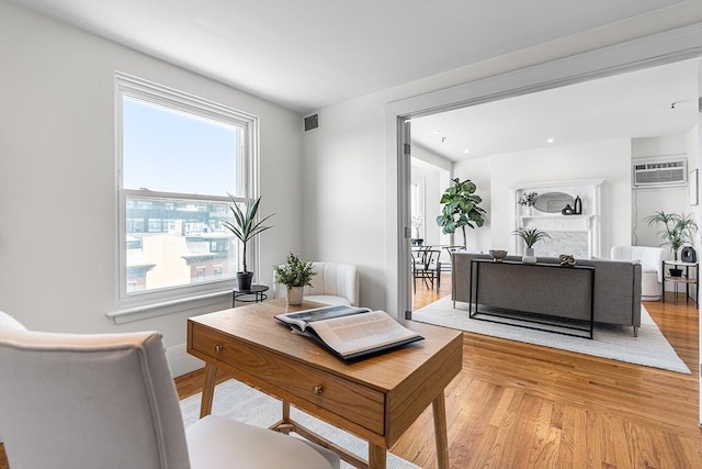 office featuring a wall mounted AC, light wood-type flooring, and visible vents