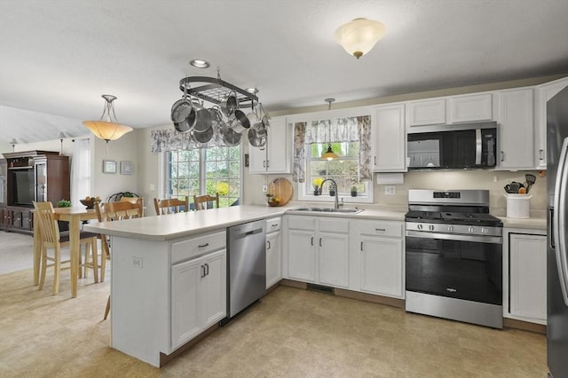 kitchen with a sink, light floors, appliances with stainless steel finishes, and a peninsula