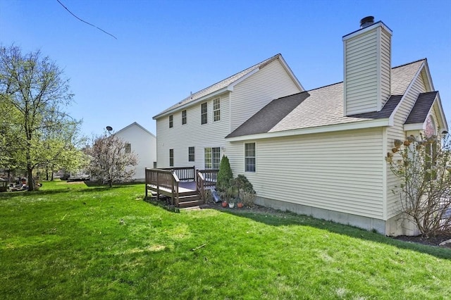 back of property featuring a lawn, a shingled roof, a wooden deck, and a chimney