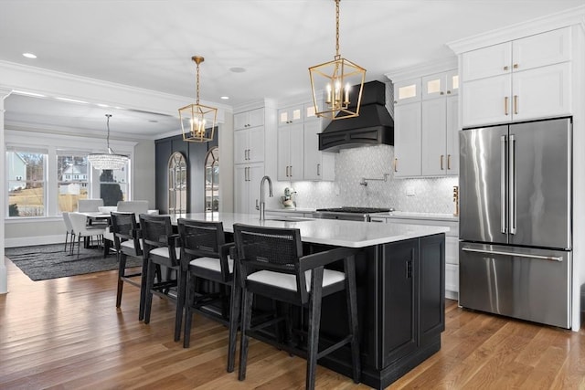 kitchen with premium range hood, an island with sink, light countertops, ornamental molding, and high quality fridge