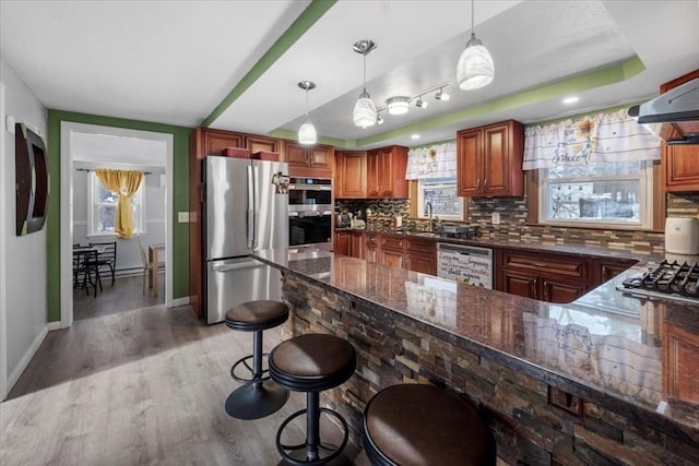 kitchen with a breakfast bar area, hanging light fixtures, hardwood / wood-style floors, stainless steel appliances, and tasteful backsplash