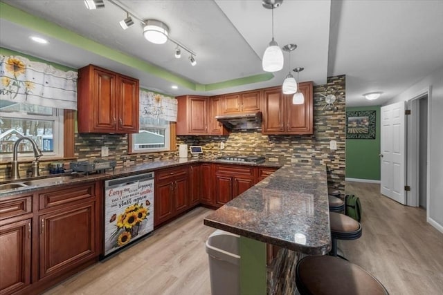 kitchen featuring a kitchen bar, sink, decorative light fixtures, dishwashing machine, and dark stone counters