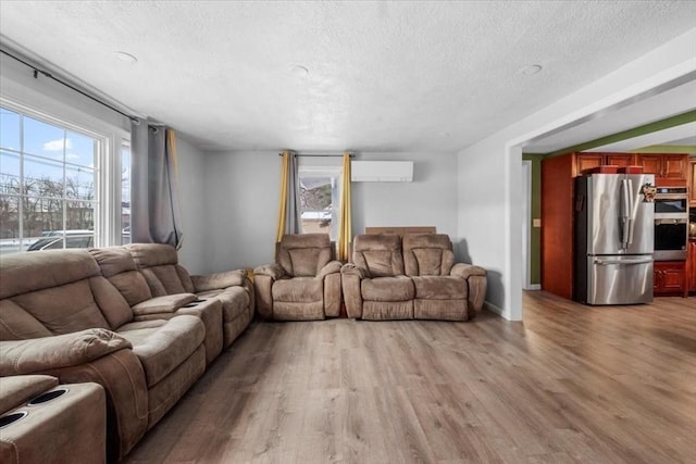 living room with a wall unit AC, light hardwood / wood-style flooring, and a textured ceiling