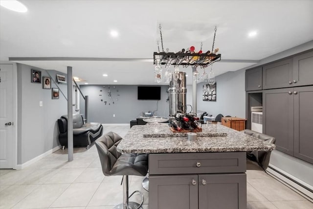 kitchen featuring a kitchen island, gray cabinetry, a kitchen breakfast bar, light tile patterned floors, and light stone countertops