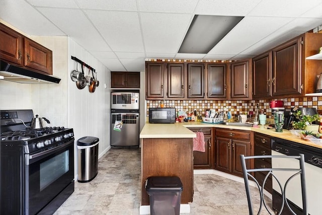 kitchen with light countertops, a paneled ceiling, backsplash, under cabinet range hood, and black appliances