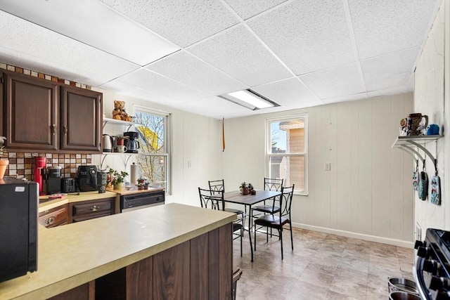 kitchen featuring light countertops, plenty of natural light, a drop ceiling, and dark brown cabinets