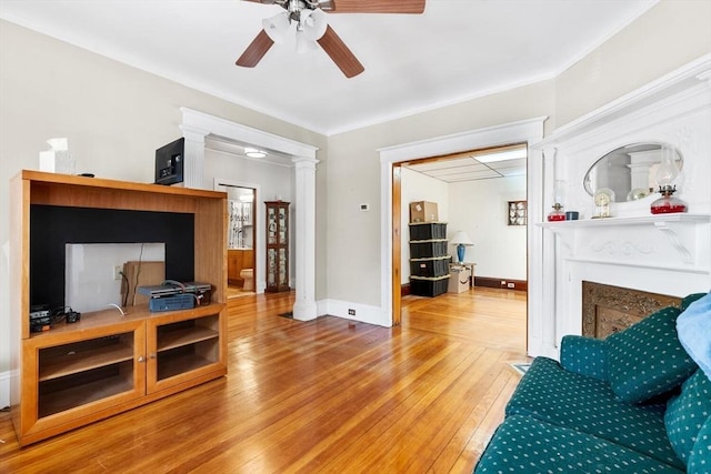 living room featuring ceiling fan, decorative columns, a fireplace with flush hearth, ornamental molding, and hardwood / wood-style floors