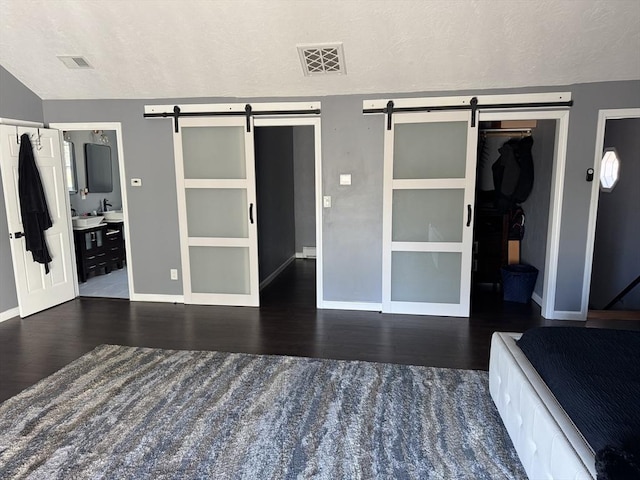 unfurnished bedroom featuring visible vents, a textured ceiling, a barn door, and wood finished floors