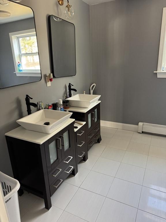 bathroom featuring a baseboard heating unit, two vanities, baseboards, and a sink