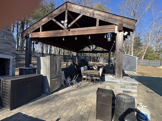 view of patio / terrace featuring fence, a shed, a gazebo, exterior fireplace, and an outbuilding