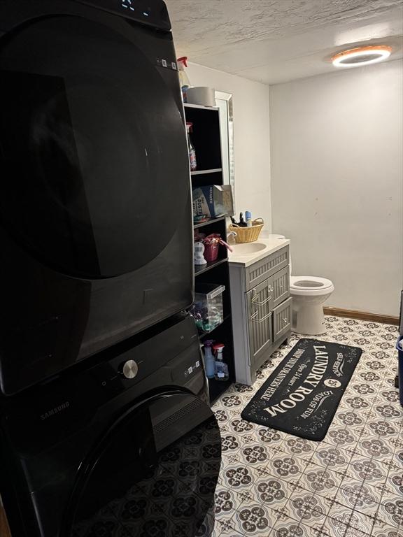 bathroom with vanity, tile patterned flooring, stacked washer and clothes dryer, a textured ceiling, and toilet