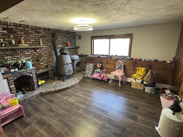 interior space featuring a textured ceiling, a fireplace with raised hearth, wood finished floors, and a wood stove