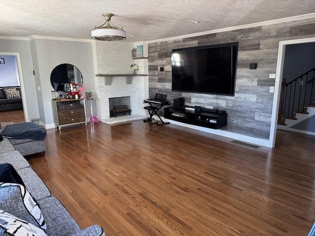 living room with visible vents, a brick fireplace, wood finished floors, and crown molding