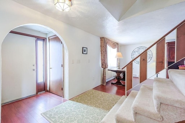 entryway with arched walkways, stairway, baseboard heating, and wood finished floors