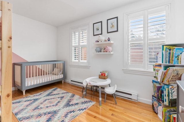 bedroom with a crib, wood finished floors, baseboards, and baseboard heating