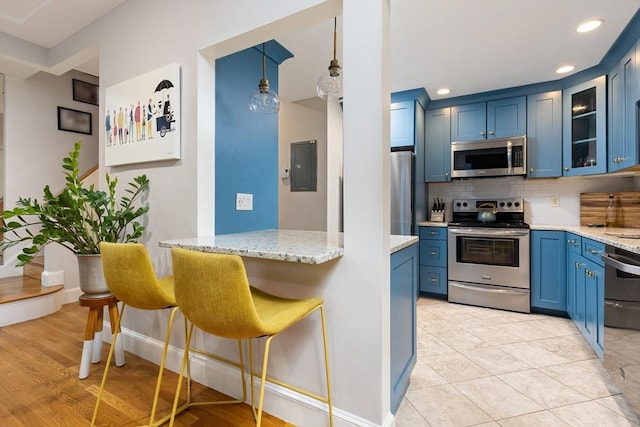 kitchen with glass insert cabinets, a breakfast bar, decorative backsplash, stainless steel appliances, and blue cabinets