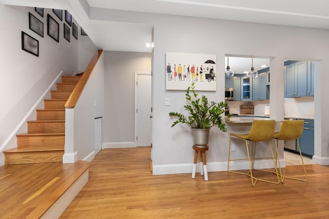 interior space with light wood finished floors, stainless steel microwave, blue cabinetry, a peninsula, and a kitchen breakfast bar