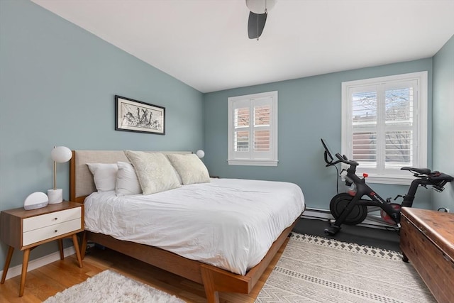 bedroom with a baseboard heating unit, baseboards, wood finished floors, and a ceiling fan