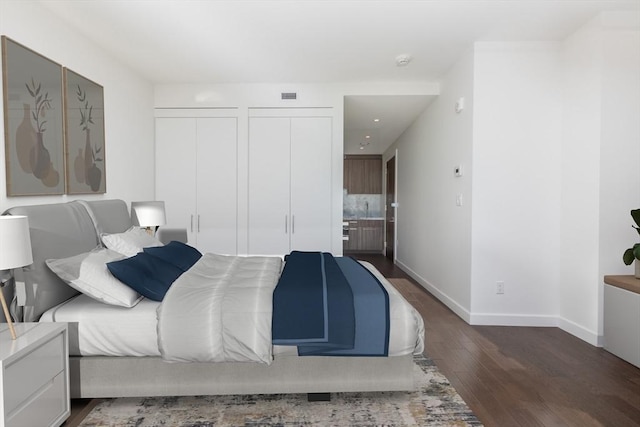 bedroom featuring wood finished floors, two closets, and baseboards