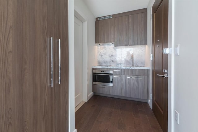 kitchen featuring stainless steel oven, modern cabinets, dark wood-style flooring, a sink, and refrigerator