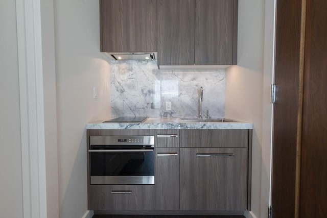 kitchen featuring modern cabinets, stainless steel oven, a sink, backsplash, and under cabinet range hood
