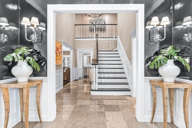 foyer entrance featuring stairway, wainscoting, a towering ceiling, and a decorative wall