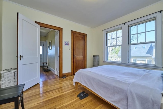 bedroom with baseboards, ornamental molding, light wood finished floors, and radiator heating unit