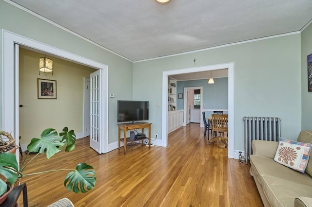living room featuring baseboards, ornamental molding, radiator heating unit, and light wood finished floors