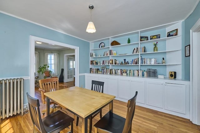 dining space featuring built in features, radiator, ornamental molding, and light wood-type flooring