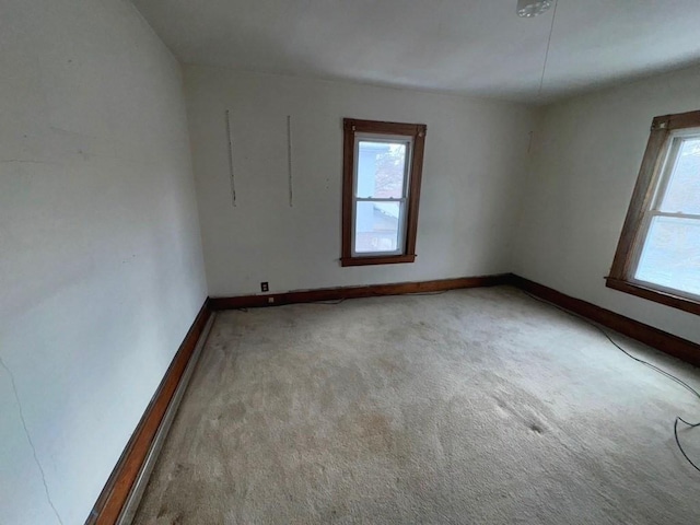 unfurnished room with a wealth of natural light, light carpet, and baseboards