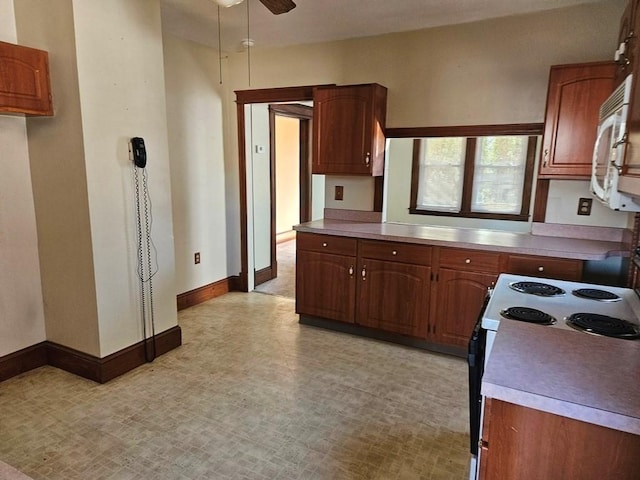 kitchen with baseboards, brown cabinetry, electric stove, white microwave, and light countertops