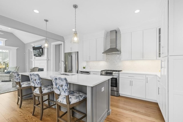 kitchen featuring a kitchen breakfast bar, wall chimney range hood, an island with sink, and appliances with stainless steel finishes