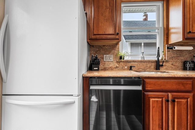 kitchen with freestanding refrigerator, stainless steel dishwasher, a sink, backsplash, and brown cabinets