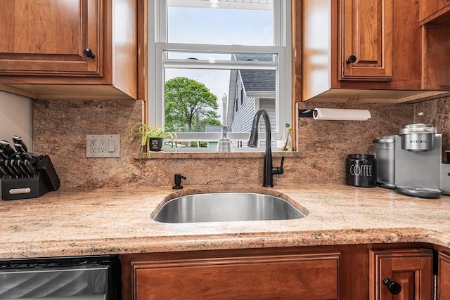 kitchen featuring a sink, decorative backsplash, brown cabinetry, dishwasher, and light stone counters