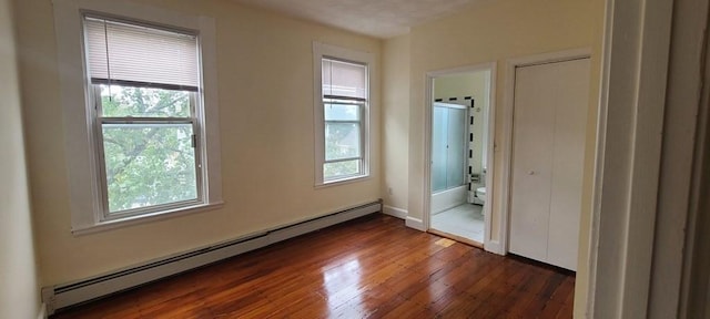 unfurnished bedroom featuring baseboard heating, connected bathroom, dark hardwood / wood-style flooring, and multiple windows