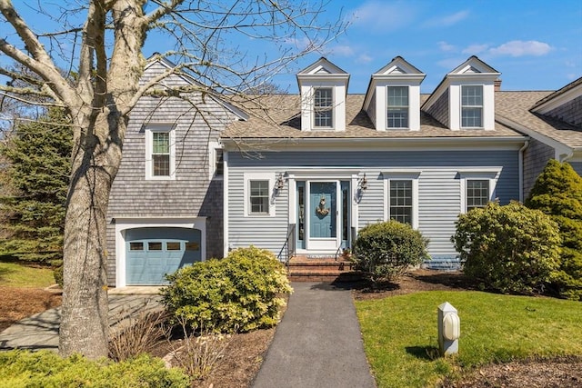 cape cod house featuring an attached garage, a shingled roof, driveway, and a front yard