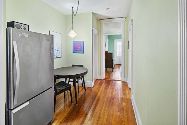 kitchen with wood-type flooring, stainless steel fridge, and hanging light fixtures