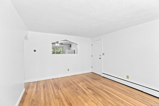 empty room featuring a baseboard radiator, arched walkways, light wood-style flooring, and baseboards