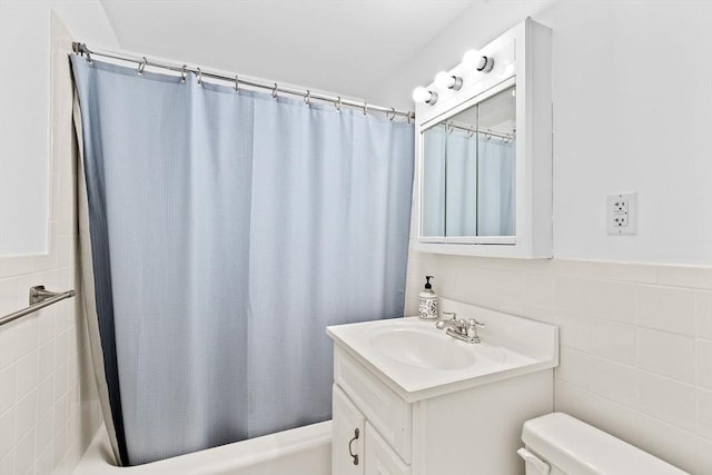 full bath with toilet, a wainscoted wall, shower / bathtub combination with curtain, vanity, and tile walls