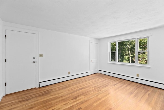 empty room with light wood-style floors, a baseboard heating unit, and a textured ceiling